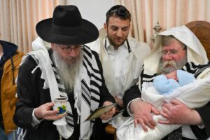 תינוק עטוף בטלית בטקס ברית מילה מרגש עם משפחתו