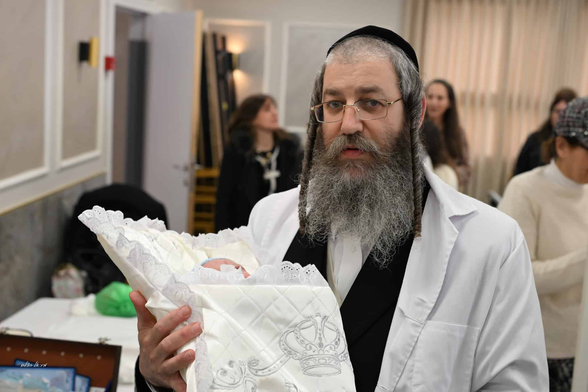 תינוק עטוף בטלית בטקס ברית מילה מרגש עם משפחתו